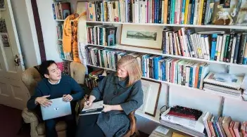Two people sitting in chairs in front of a large bookcase.