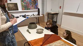 Group of people beside a table, holding a clipboard and reviewing historical objects laid out in front of them