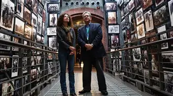 A hallway lined with pictures features two people standing together