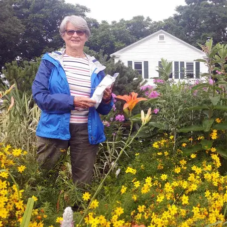 a gardener standing in a garden, smiling at the camera