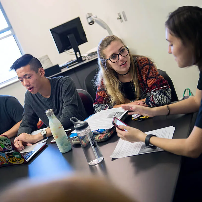 Students sit around a table having a lively class discussion