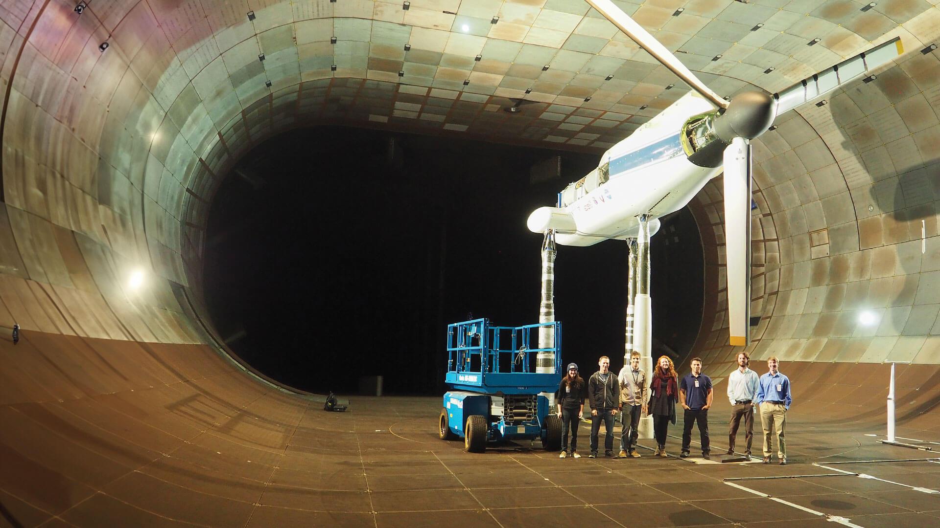 students in a group pose under a turbine in a NASA wind tunnel