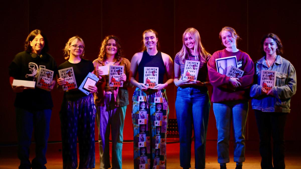 Seven students pose on the colorfully-lit stage in Brennan's Pub with their prizes after competing in Catamount Tales!