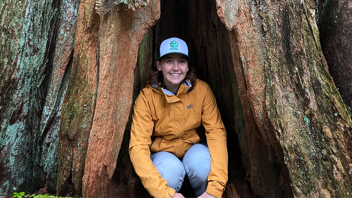 Emma Conti is smiling and kneeling inside a large tree