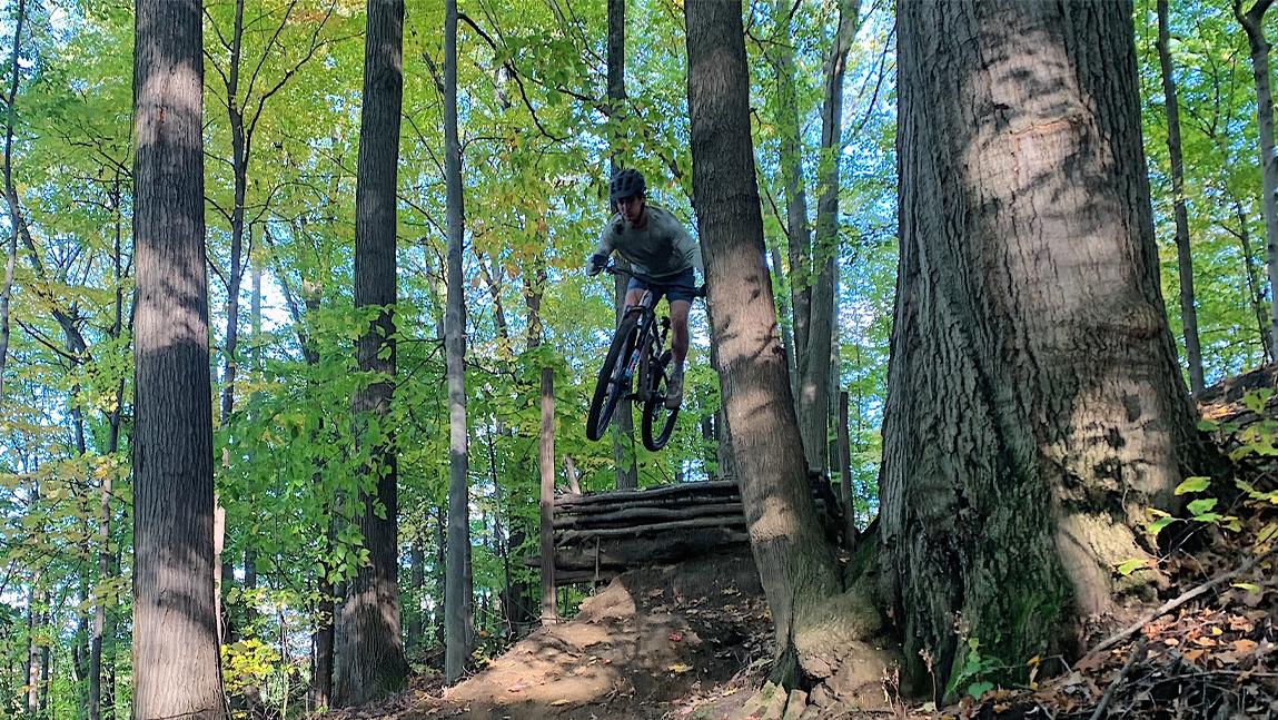 Gus performing a mountain bike jump in the forest.