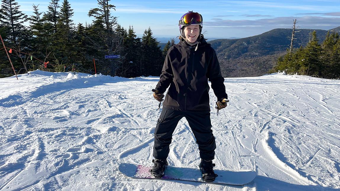 Katie Conlon stands on snowboard at top of ski resort trail.