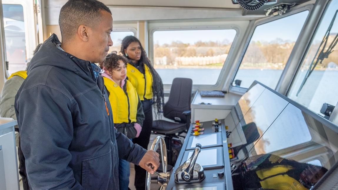 Captain Taylor Resnick at the helm of the R/V Marcelle Melosira showing the boat controls to two students