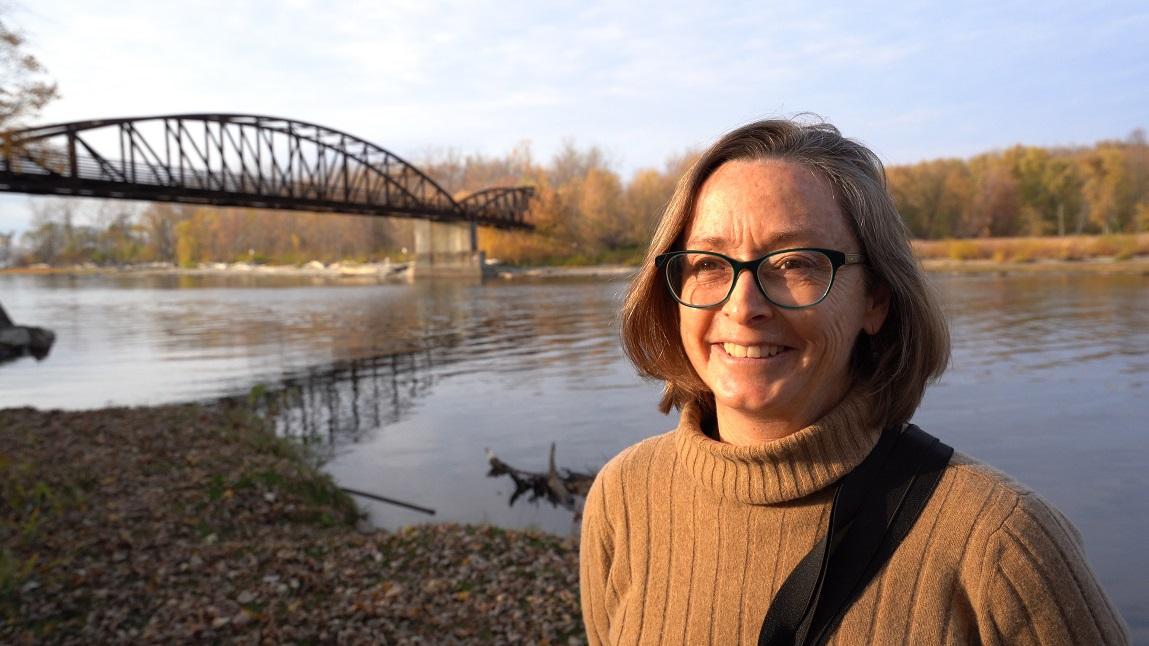 Trish O'Kane standing outside in front of a river smiling