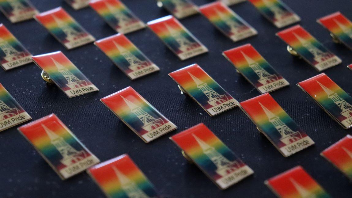 rows of rainbow pins with the UVM clock tower on them that say UVM Pride