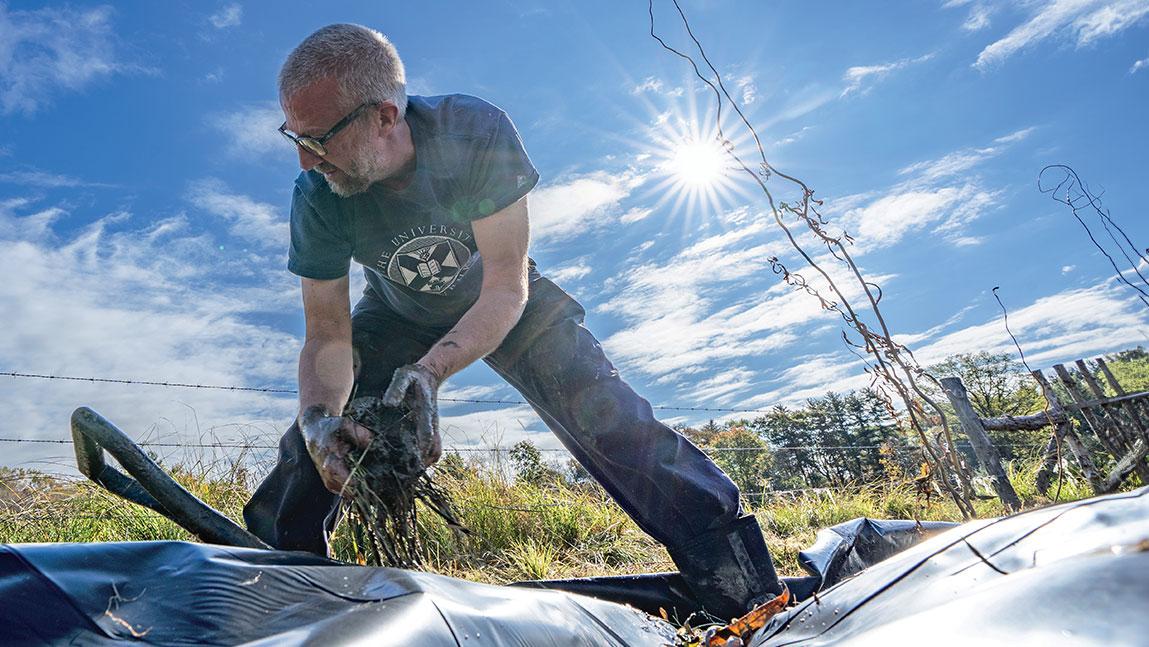 Mark Usher stands with his legs apart, hands dirty as he digs through the dirt in a field