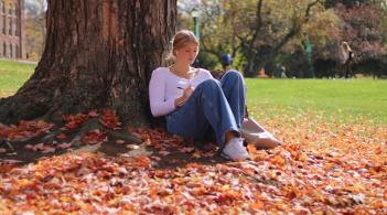 Student studies beneath a tree while sitting in orange fall leaves