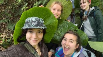 three students standing in leaves laughing at the camera