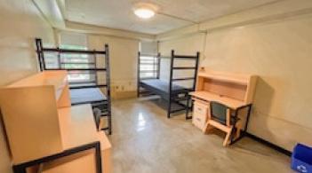 A room with two beds, two dressers, and two desks. 