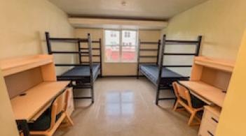 A room with two beds, two dressers/closets, and two desks.