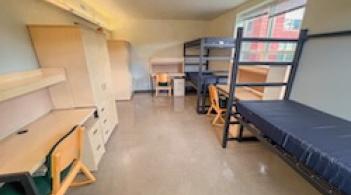 A room with three beds, three dressers/closets, and three desks.