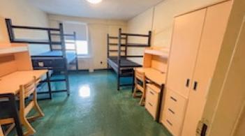 A room with two beds, two dressers, and two desks. 