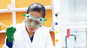 Student with goggles and lab coat holding a tube