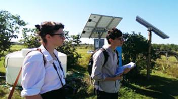 Two individuals standing in front of a solar panel taking notes