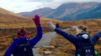 Two people joyfully lift their hands on a picturesque trail