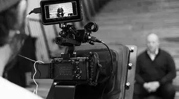 a black and white photo of a camera person shooting a sitting subject