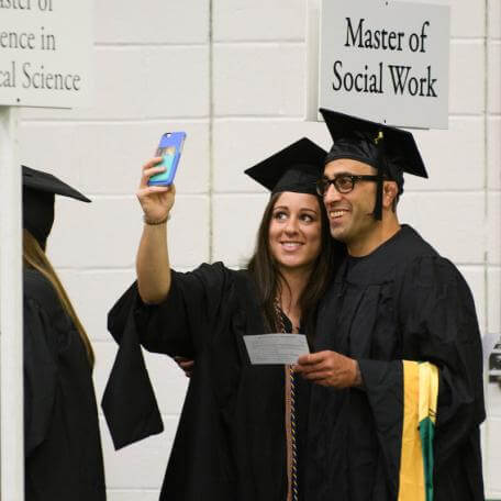 Smiling grads take selfies at commencement.
