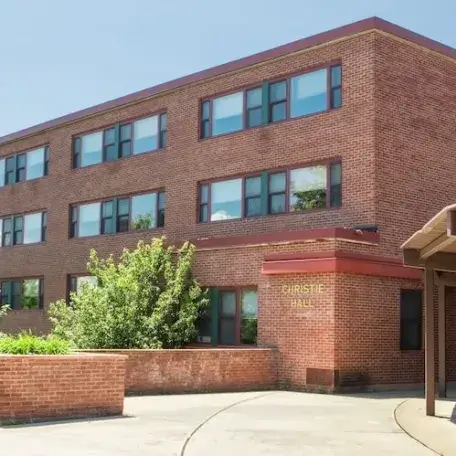 A three-story brick residence hall with trees beside it.