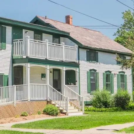 A white house with green shutters and a porch/balcony.