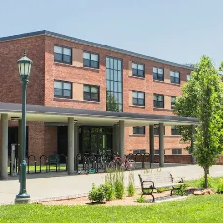 A three-story brick residence hall with a green space in front of it.