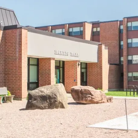 A 3-story brick residence hall with a grassy area and trees surrounding it.