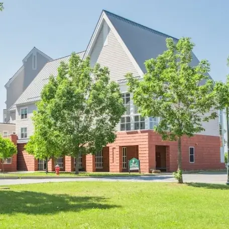 Modern, three-story residence hall with trees and grassy area.