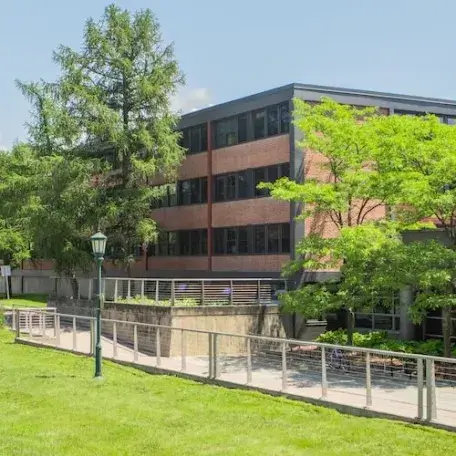 A four-story, brick residence hall with trees and a grassy area in front of it.