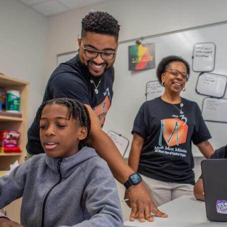 Daniel Fairley G'16 smiles and he works with students in a classroom.