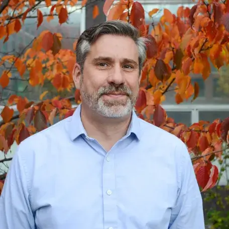 A person wearing a blue shirt standing in front of a tree