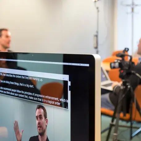 A flatscreen monitor shows live-captions of an interview taking place in the background