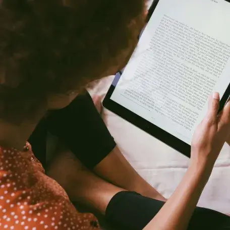 A Black student reads large text on a tablet while sitting cross-legged