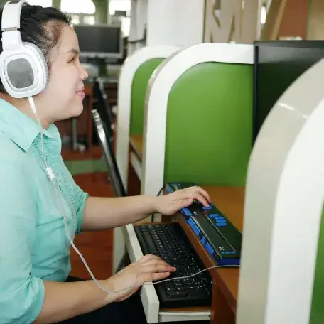 A Blind Asian woman works at a Braille keyboard while wearing headphones