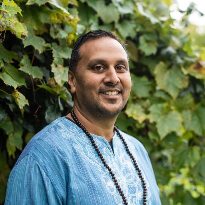 Vice Provost Amer F. Ahmed standing in front of greenery in a blue shirt