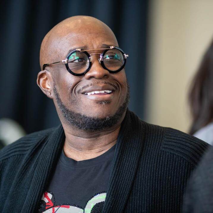 James Ross wearing stylish glasses and black cardigan smiling while looking at someone outside of the photo