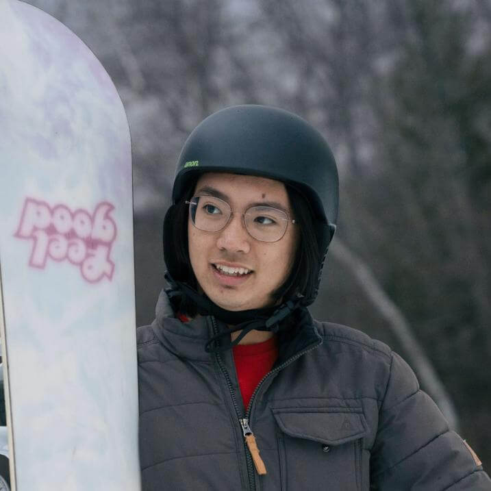 Jonah wearing a helmet and winter coat holding a snowboard