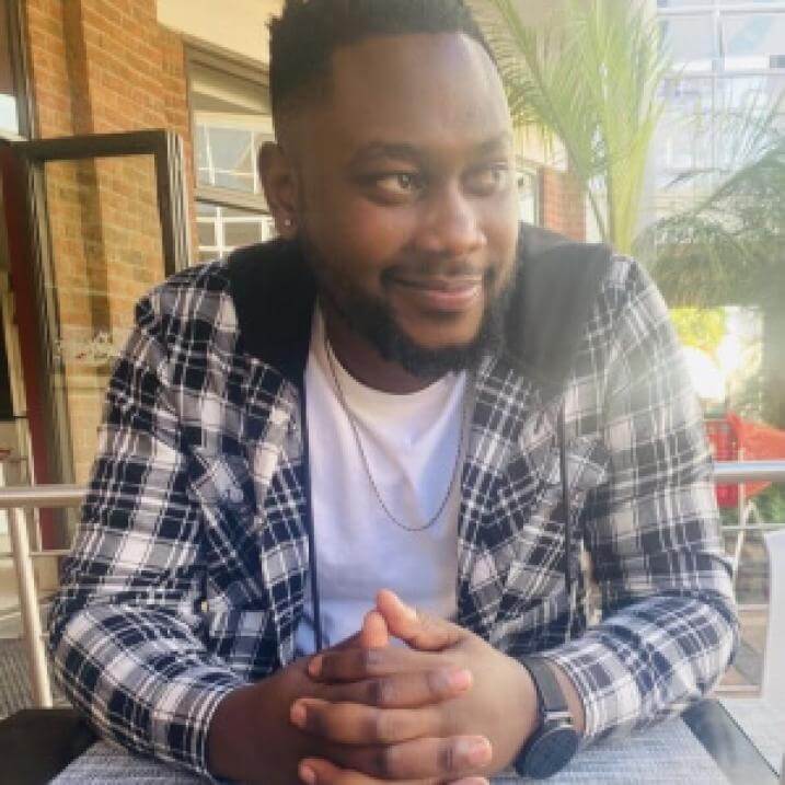 Taku smiling and sitting at a table outdoors wearing a flannel shirt and white t-shirt