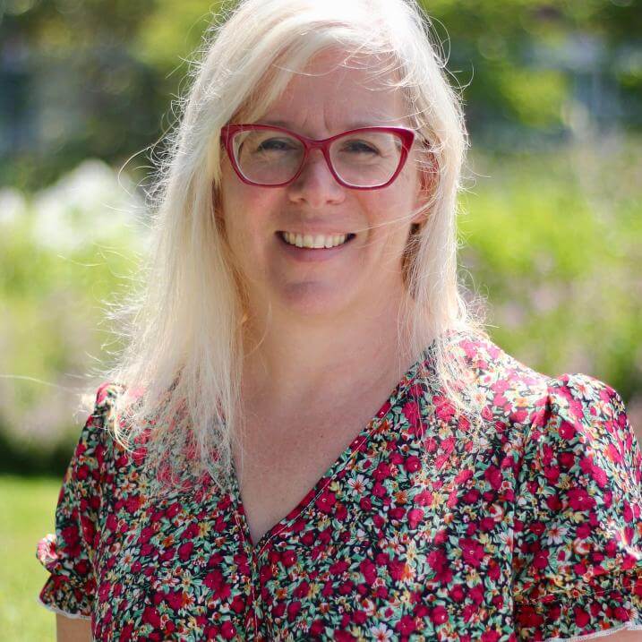 Photo of Lina smiling on the Davis Center green, in a red floral dress and matching red glasses