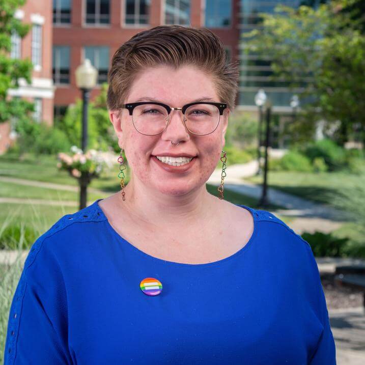 alex martin in a blue shirt wearing glasses and a pride pin