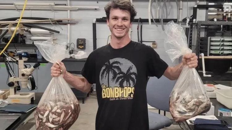Pierre standing in a lab and holding two full bags of fish.