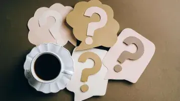 Cup of coffee with paper question mark cutouts.