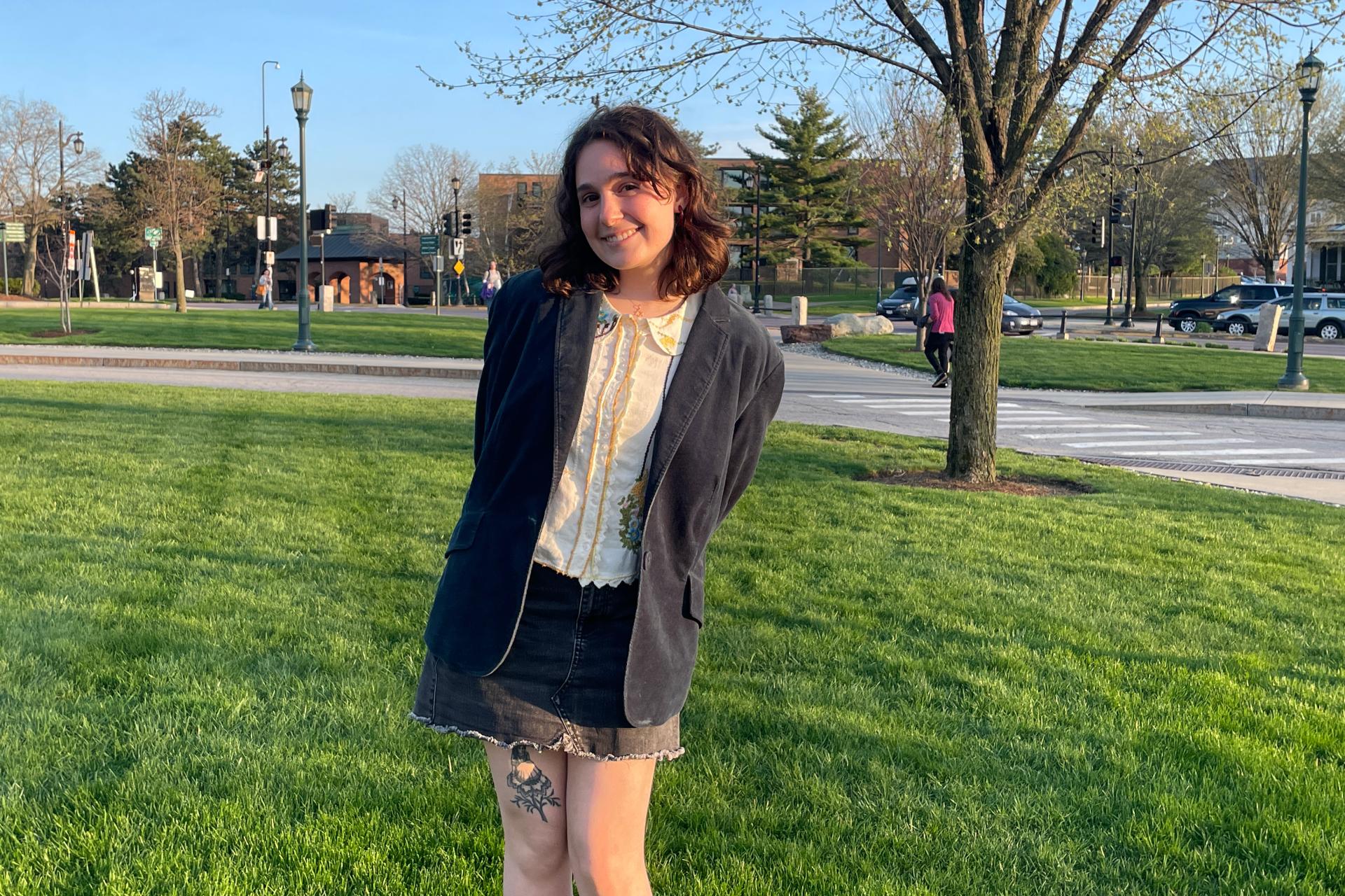 young woman in blazer standing on grass on UVM campus on sunny day