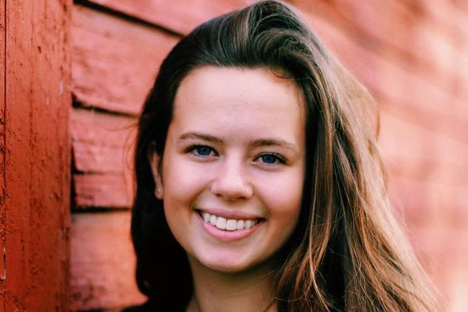 Closeup of student Annabelle Collins by wood-sided building, smiling