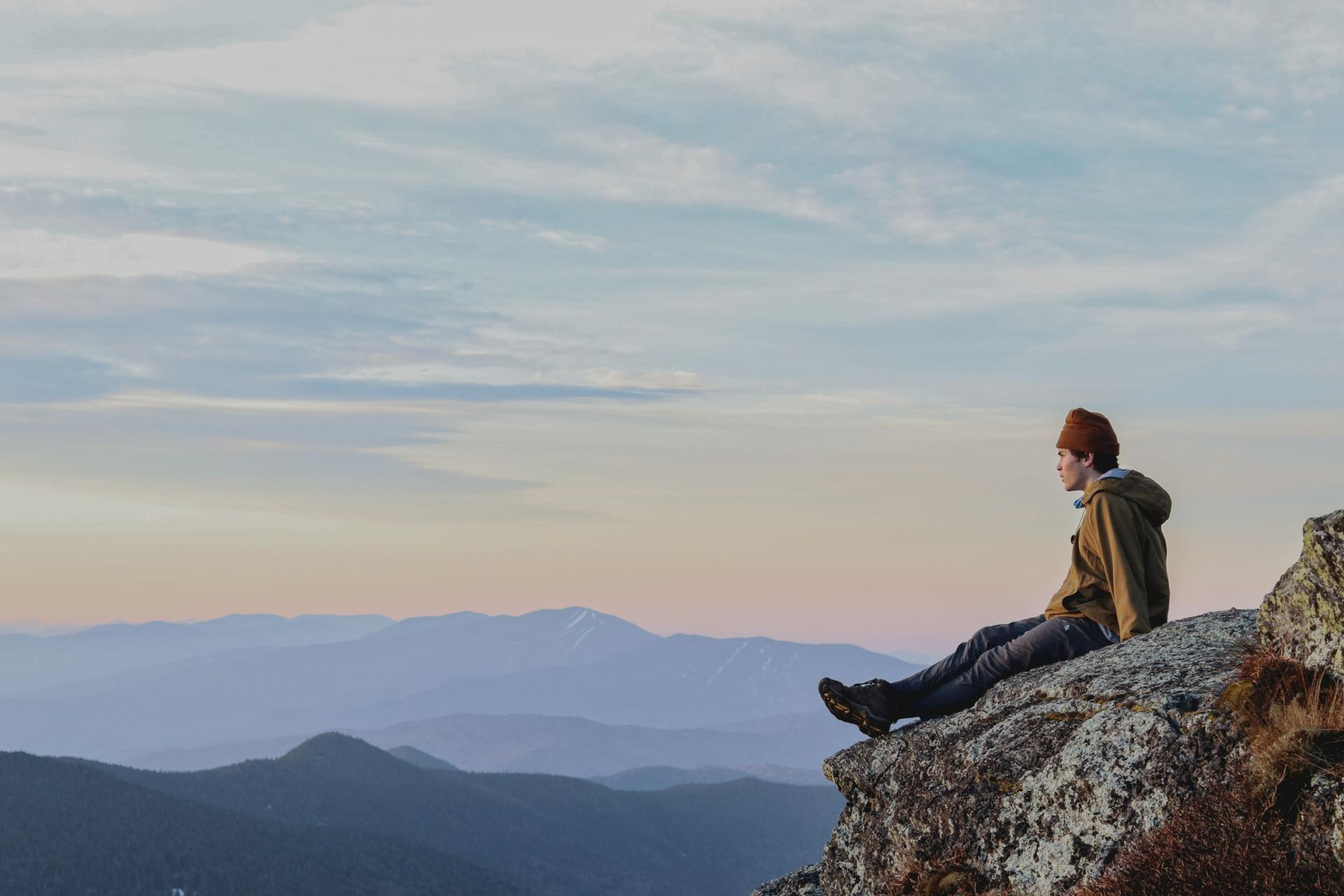 young man sitting on mountaintop with broad mountain vista