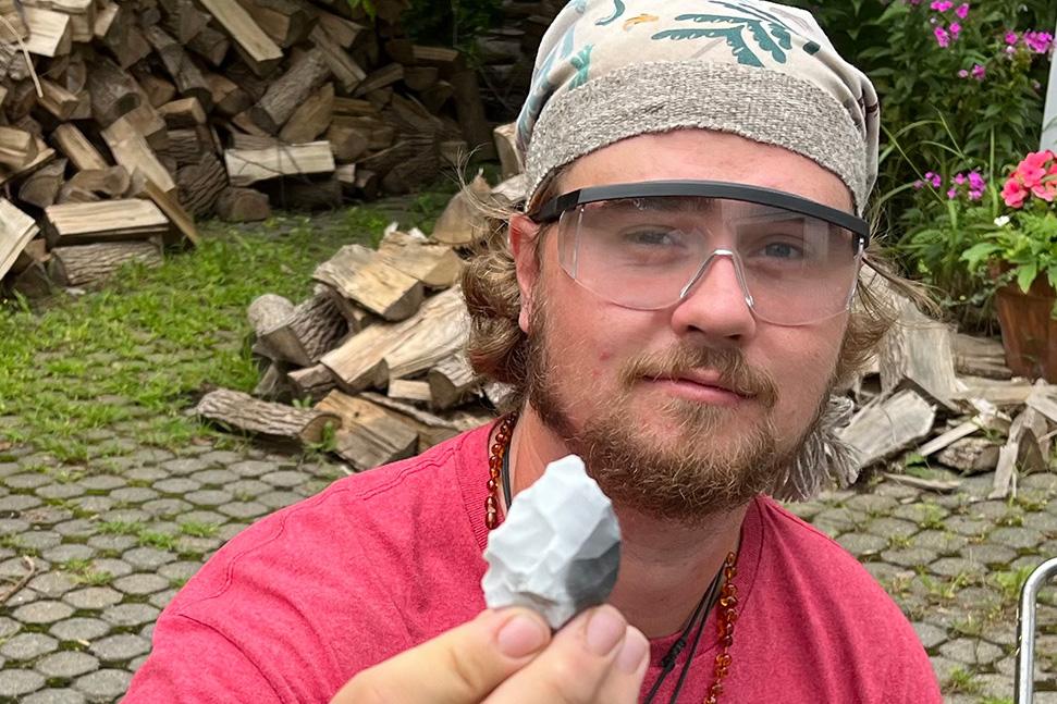 young man with beard, safety glasses, bandana, and pink shirt holding up a chiseled fossil rock