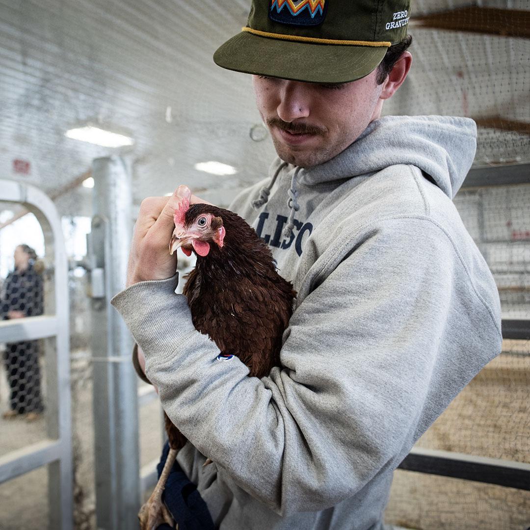 student in a hat holds a chicken