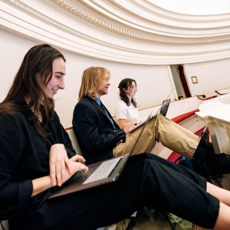 Three people sit together while looking at their laptops.